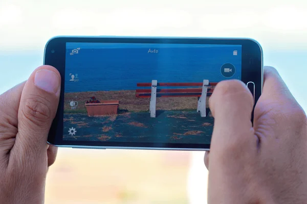 Close up on male hands taking photo of sea coast with mobile cell phone. Summer beach holiday vacation concept