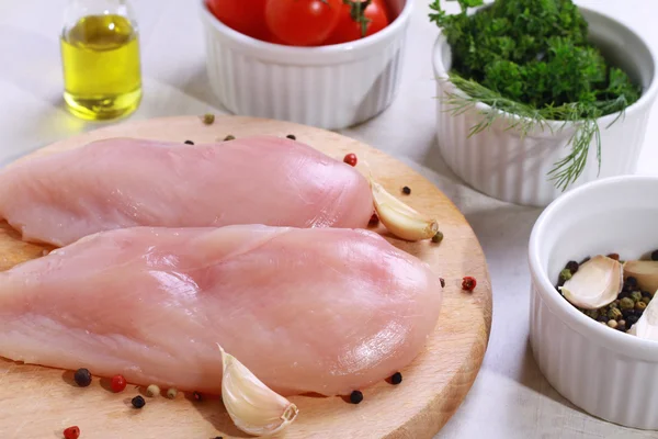 Raw chicken breast fillets decorated with salad, olive oil and cherry tomatoes on wooden cutting board. Diet food, healthy lifestyle