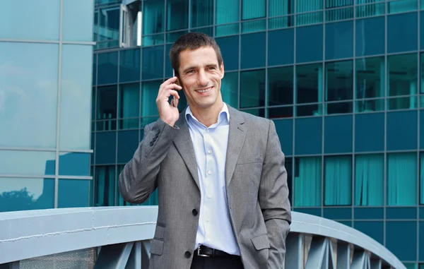 Young handsome, successful businessman talking on the phone in the city, in front of modern building