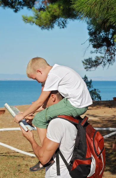 Father giving his son piggyback ride outdoors. Man and boy son looking at map infront of sea, active summer holiday vacation, family travel photo