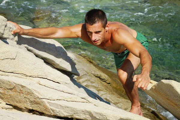 Man climbing on mountain rocks against sea water. Extreme sports outdoors. Active summer vacation