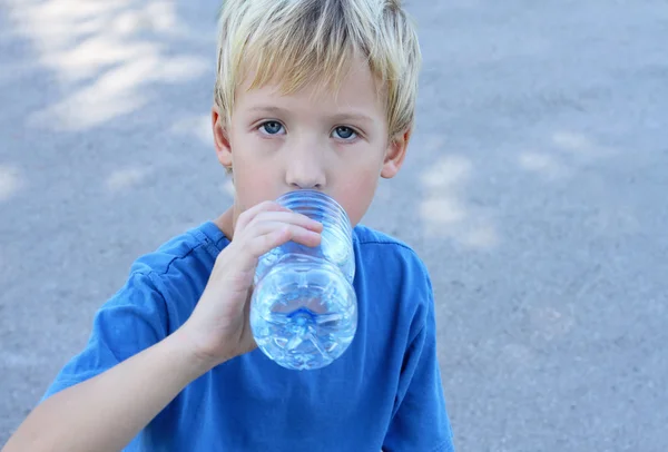 Outdoor portrait of 5 year old boy drinking water from bottle in park. Kids, fun, sport, summer, active vacation