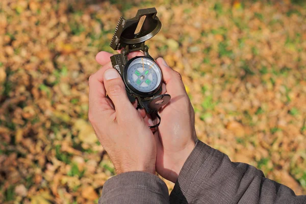Man using compass in nature or autumn forest. Close up of hands