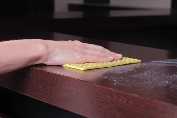 Close up of  hand cleaning wooden table with furniture polish. Using yellow sponge for cleaning dusty wood. House  cleaning and home hygiene concept