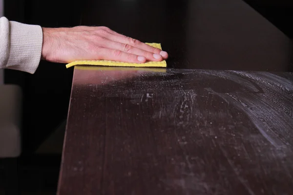 Close up of male hand cleaning wooden table with furniture polish. Using yellow sponge for cleaning dusty wood. House cleaning and home hygiene concept