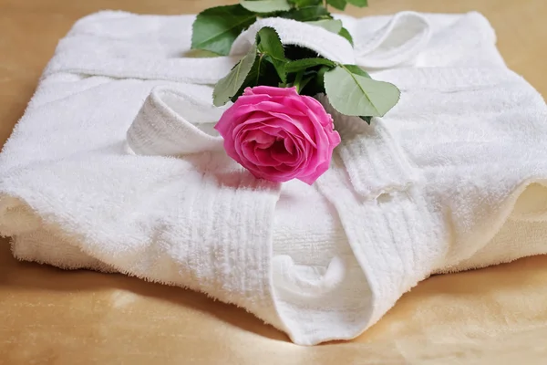 Stack of white  and soft hotel towels and bathrobe decorated with rose flower. Perfect white laundry. Spa, healthy lifestyle and relaxation concept.