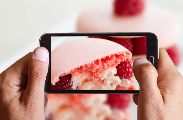 Male hand taking photo of macarons cakes with raspberry with cell, mobile phone.