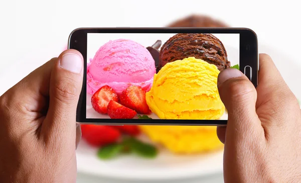 Male hand taking photo of ice cream with strawberry with cell, mobile phone.