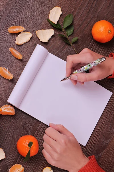 Winter Time  and Christmas background. Mandarins and blank paper on wooden background, copy space image Close up on female hands writing wish list for new year, woman writing  new year goals