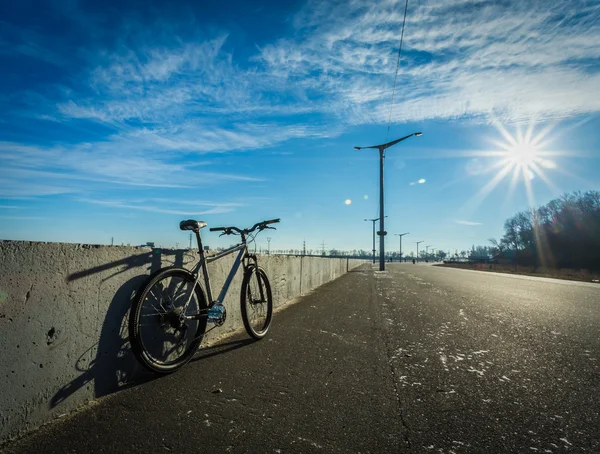 Bicycle stands at the side of the road on a sunny day, empty road, sun glare, blue sky, vignette