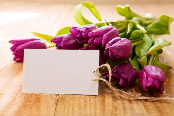 Purple tulips with white card on wood background.