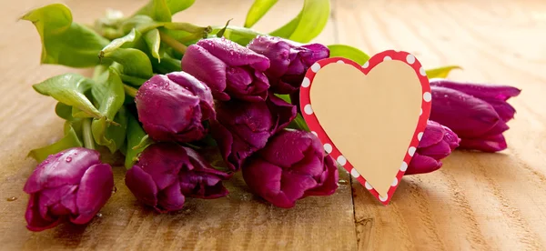 Purple tulips with heart card on wood background.