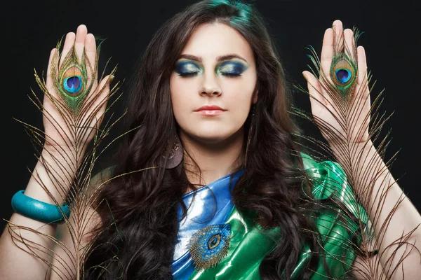 Psychic abilities psychics communicate with spirits. Beauty portrait of girl holding peacock feathers, bright clothes, creative makeup.