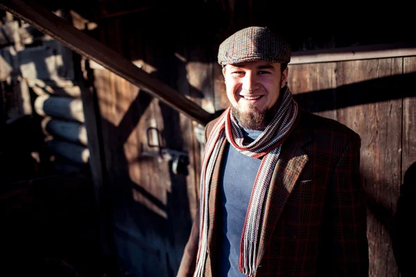 Man in flat cap with old-fashioned outfit outdoors on  background of wooden constructions.