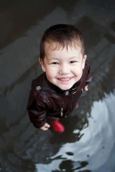 Boy in rubber boots plays at a puddle.