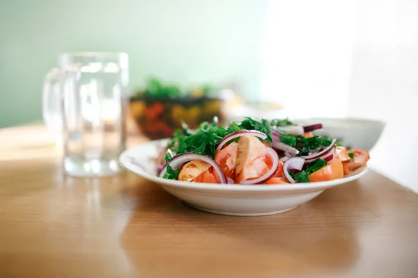 Fresh mixed vegetable salad of tomatoes, onions and parsley. Empty glass mug in the background. Healthy simple food, vitamins during harsh living conditions, economy. Natural light, selective focus.