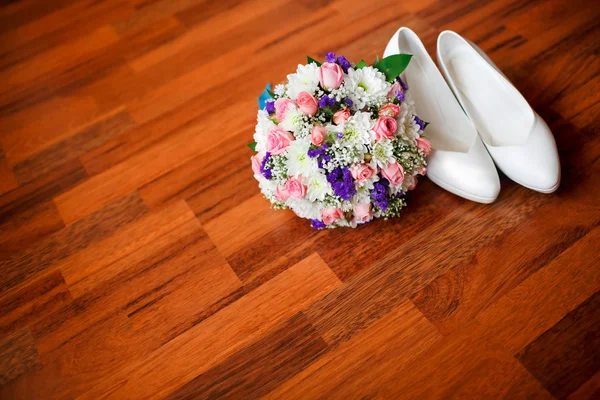 Wedding bouquet with violet flowers and white brides wedding shoes on the parquet floor, room for copy. Bridal accessories.
