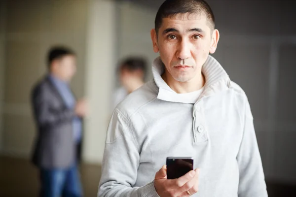 Middle Asian man short haircut with phone in his hand questioning look directly into camera, gets a job. Against background of business men discussing employment. Unemployment, human resources.