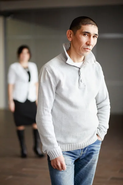 Middle aged man in casual clothes with short hair thoughtfully looking directly into camera, the employee gets job. In background, HR Director woman wearing white suit and strict black dress waits.