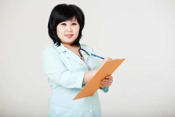 Asian brunette nurse with stethoscope around neck and folder in her hands ready to record patient information, provides diagnosis. Registry, medical data entry, record. On reception at doctor.