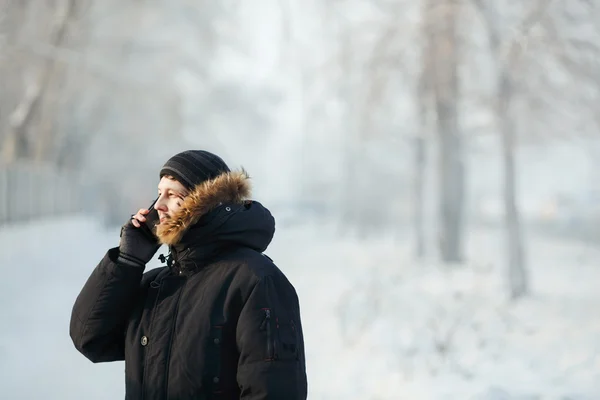 Siberian man talking on the phone outdoors by cold day in a warm winter down jacket with fur hood. Snow frost, communication at any weather. Place for your text.