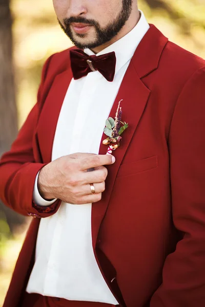 Boutonniere geared to buttonhole. Groom in red suit with stylish beard and mustache.