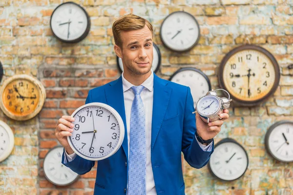 Man in suit standing near wall with clocks