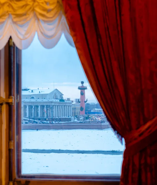 Views of the snow-covered winter town from the window, curtained by red curtains