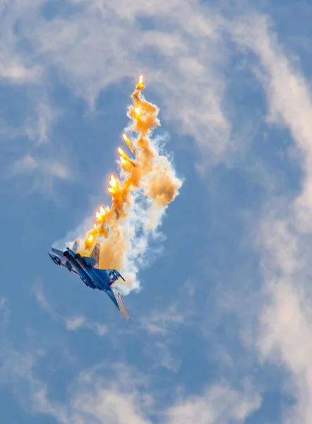Military aircraft fighter SU-27 performs the maneuver with the ejection of heat missiles, releasing a plume of hot gases.