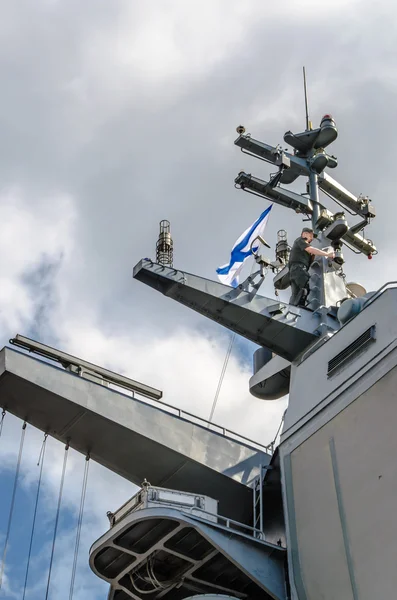 Military naval officer runs high on the mast of a warship on a background of clouds