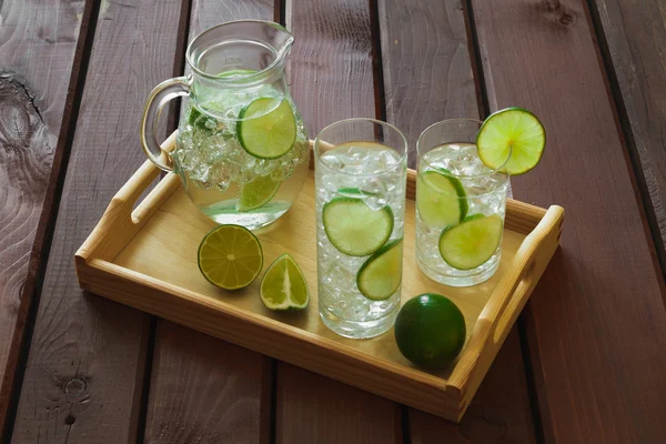 Two drinks and jug on wooden tray with ice and condensation on g