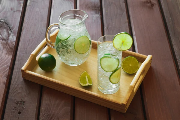 Drink and jug on wooden tray with ice and condensation on glass