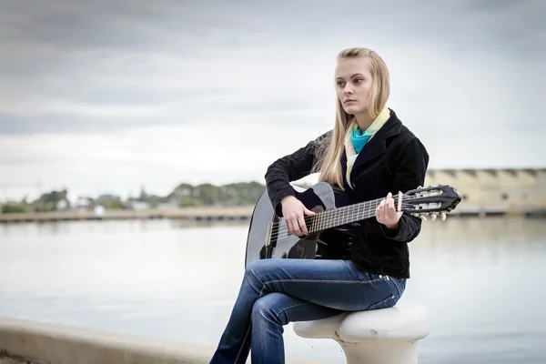 Cute blonde playing guitar while sitting on the bitt