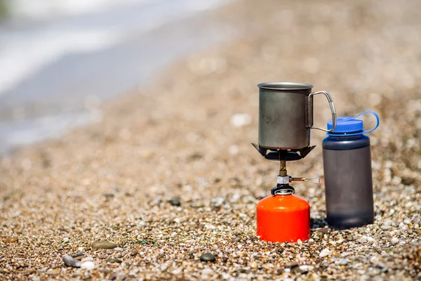 Gas stove, titanium mug and water plastic bottle outdoor on sea shore