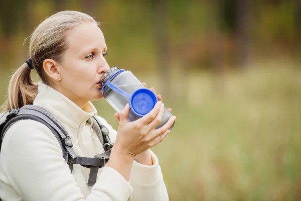 Young woman drinking water with backpack at forest valley