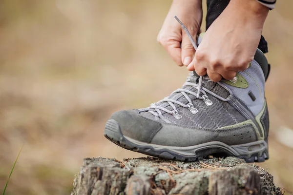 Woman on a hiking trail ties the shoelace on her walking shoe,