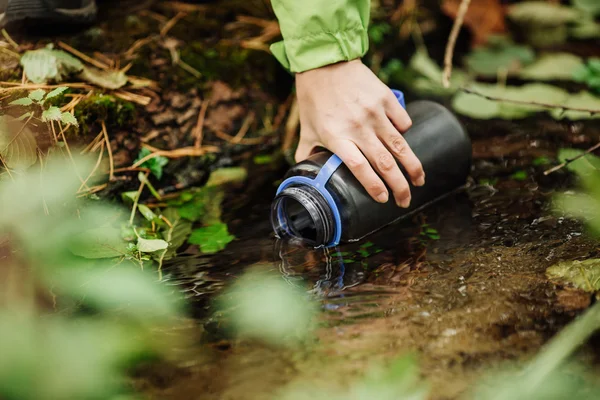Woman taking water from forest spring on hiking trip