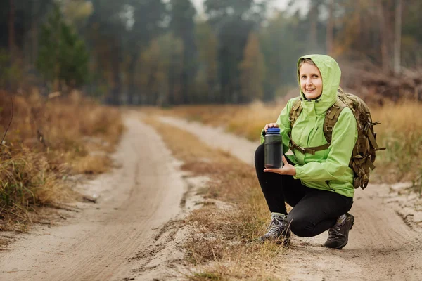 Young woman drinking water with backpack at forest valley