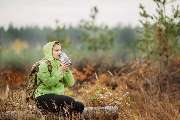 Young woman drinking water with backpack at forest valley