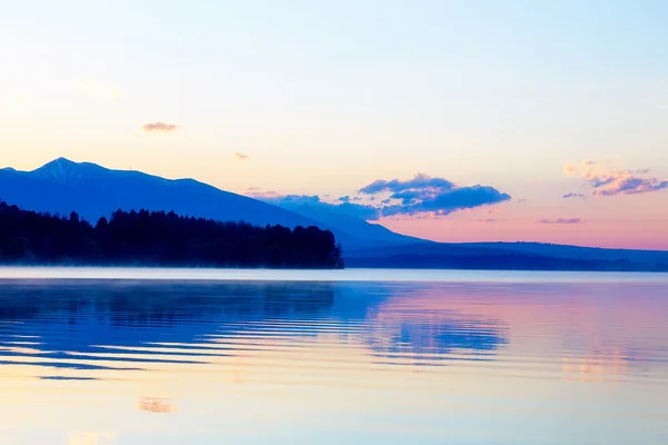 Beautiful landscape with mountains and lake at dawn in golden, blue and purple tones.