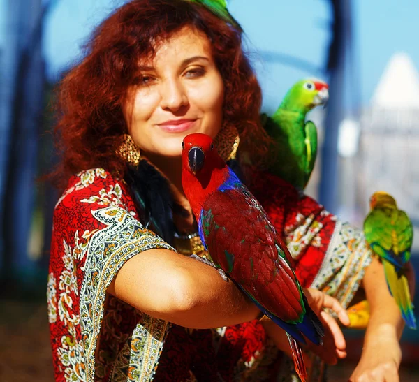 Young woman in ornamental dress and beautiful gold jewelry with a color parrots