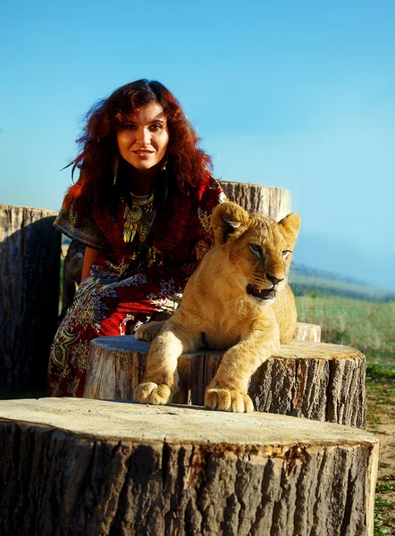 Young woman with ornamental dress and gold jewel playing with lion cub in nature.