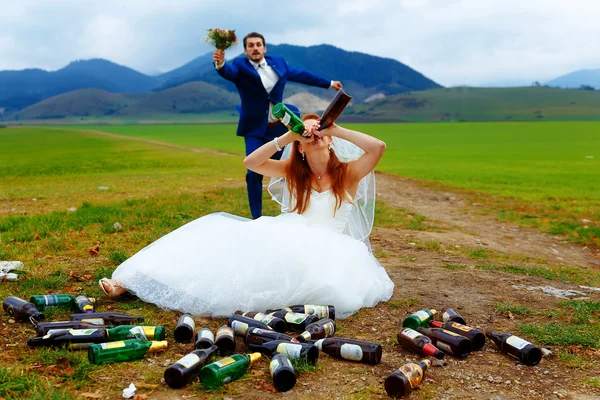 Drunken bride with lots of empty beer bottles in mountain landscape  and groom comming to her- funny wedding concept.