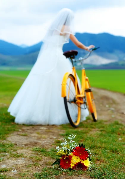 Bride on orange bike in beautiful wedding dress with lace in landscape. with wedding bouquet. wedding concept.