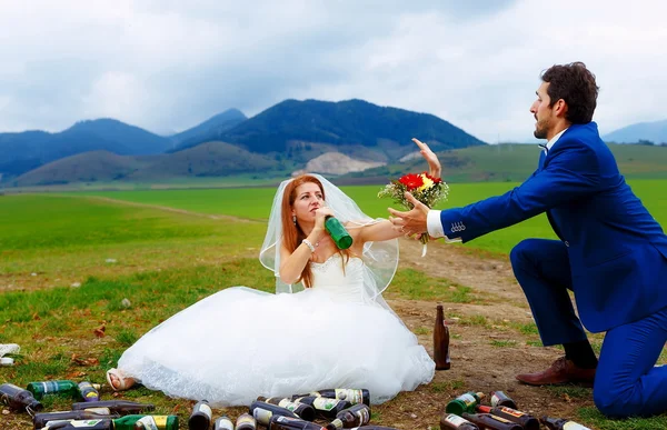 Drunken bride with lots of empty beer bottles in mountain landscape  and groom comming to her- funny wedding concept.