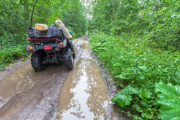 The dirty ATV stands with bags and stuff in the deep muddy puddle on the forest road