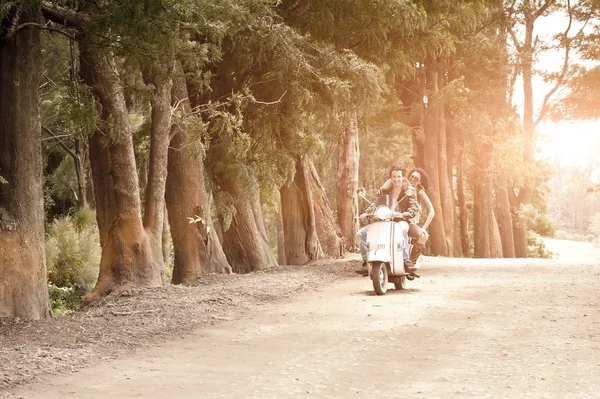 Young happy couple enjoying an afternoon ride on scooter on dirt road