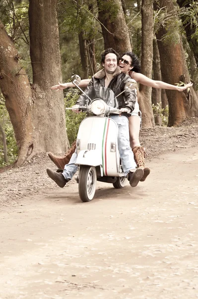 Young attractive couple traveling by scooter along dirt road