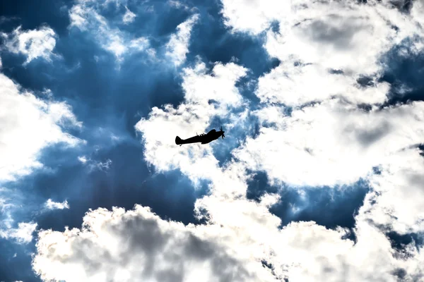 Spitfire silhouette on dark blue sky and snow white clouds