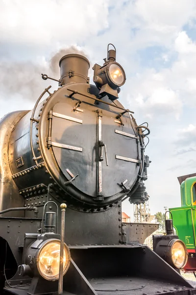 Old steam engine, front view with yellow lights, smoking